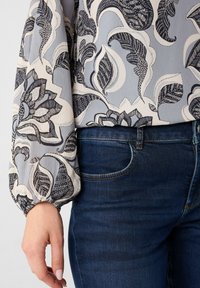 Bluse mit Blumenmuster in Hellblau und Creme, mit lockeren, puffigen Ärmeln. Kombiniert mit Jeans aus dunklem Denim im klassischen Schnitt.