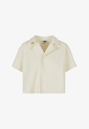 Trumpas rankovėmis, apkirptas marškinėliai pagaminti iš minkštos, smėlio spalvos medžiagos. Turi smailų apykaklę ir penkis mygtukus priekyje. Tekstūruotas paviršius.