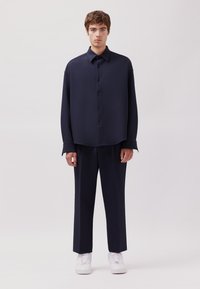 Set di camicia e pantaloni blu navale in un tessuto morbido e liscio. Caratteristiche includono una chiusura con bottoni, maniche lunghe e taglio dritto; abbinato a sneakers bianche.