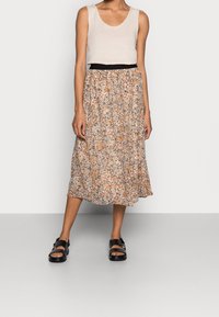 Bloemen midi rok met een elastische tailleband, voorzien van oranje, blauw en crèmekleurige patronen. Gepaard met een beige tanktop en zwarte sandalen.
