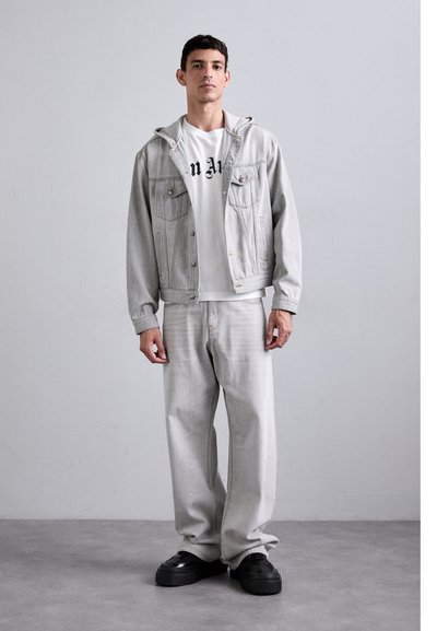 Lys grå denimjakke med hætte, to frontlommer, parret med matchende lys grå bukser og sorte platform sko. Enkel design.