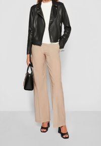 Černá kožená motocyklová bunda, bílý top s kulatým výstřihem, béžové široké kalhoty a černé otevřené podpatky. Černá kabelka s minimálními zdobeními.