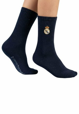 Nogi w czarnych żebrowanych skarpetkach z logo Realu Madryt na górnej części oraz napisem "LaLiga Real Madrid" na podeszwie.