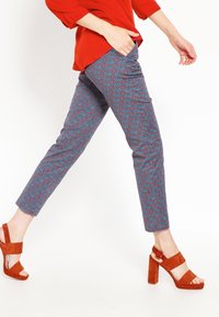 Pestrobarevné kalhoty se geometrickým vzorem v odstínech modré a červené, zkombinované s červenými suede sandály na blokovém podpatku.