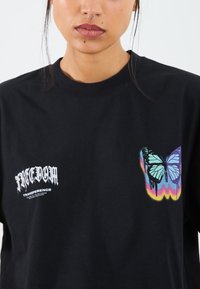 Black cotton t-shirt featuring white text that reads "FREEDOM TRANSFERENCE" and a colorful butterfly graphic with a gradient background.