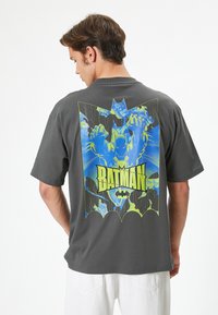 Camiseta de algodón gris con una gran impresión gráfica de Batman en azul y verde en la parte posterior; de mangas cortas y corte relajado.