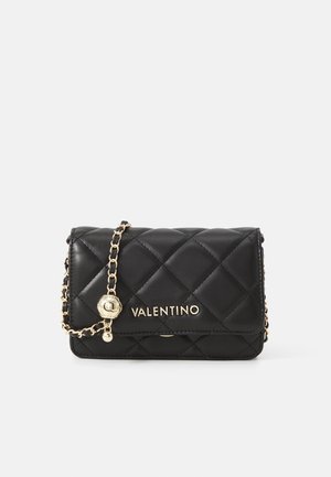 Zwarte doorgestikte Valentino handtas met een gouden kettingriem en logo aan de voorkant, tegen een effen lichte achtergrond.