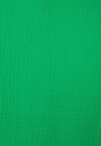 Tissu vert vif à surface texturée, présentant des plis subtils et une coloration uniforme sans motifs ni accents.