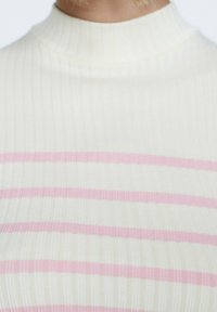 Krämfärgad stickad topp med hög krage som har horisontella ljusrosa ränder. Tyget har en räfflad textur.