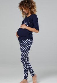 Maternity outfit with a navy top featuring a heart pattern and button detail, paired with navy leggings adorned with white hearts.