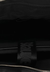 Interno di una borsa in tela nera con chiusura a zip. Presenta un'etichetta tessuta con del testo e una superficie liscia. Foderato in un materiale nero simile.