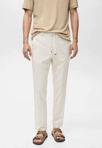 Light beige cotton blend pants with vertical stripes, elastic waistband, drawstring closure, and side pockets. Paired with brown sandals.