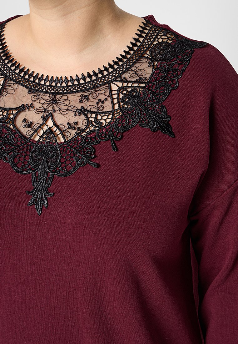 Top bordeaux con dettagli in pizzo nero intrecciato sul colletto, con motivi floreali e un aspetto di tessuto testurizzato.
