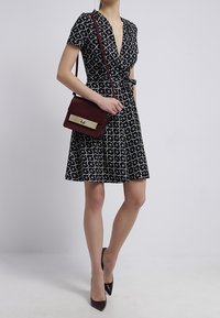 Svart indress med ett geometriskt mönster i blått och gult, i kombination med en vinröd handväska med ett guldspänne och högklackade skor.