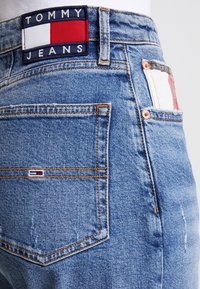 Denimjeans med en ljusblå tvätt, kopparstickningar och en TOMMY JEANS-logopatch med röda, vita och marinblå accenter på midjebandet.