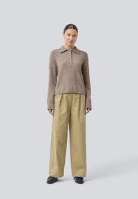 Brun strikket genser med krage og tre-knappers placket, kombinert med beige vide bukser. Teksturen er myk, med en avslappet passform.