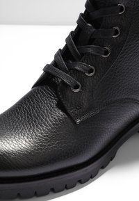 Botte en cuir noir texturé avec une semelle en caoutchouc épaisse et des lacets noirs passés à travers des œillets en métal.