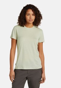 Helles grünes T-Shirt mit kurzen Ärmeln und rundem Halsausschnitt, glatter Textur und lässiger Passform. Etikett auf der linken Seite nah dem Saum sichtbar.