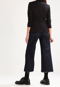 Czarna, dopasowana marynarka, ciemnoniebieskie dżinsy o szerokich nogawkach z postrzępionym wykończeniem oraz czarne buty na sznurówki. Marynarka ma dopasowane rękawy i usztywniony fason.