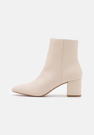Bottine beige à bout pointu, talon bloc, finition lisse et couture latérale, vue de profil sur un fond clair.