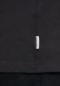 Svart texturerad tyg med ett horisontellt ribbmönster. Inkluderar en liten vit etikett med "JACK & JONES" vid botten söm.