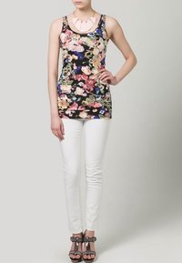 Floral-patterned black tank top, white skinny jeans, and metallic open-toe sandals. Necklace features pink geometric accents.