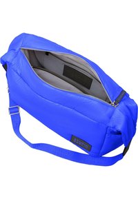 Borsa blu imbottita con chiusura a zip, interno grigio, tracolla regolabile e toppa nera con logo. Texture liscia e forma rettangolare.