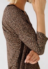 Haut en imprimé léopard brun avec manches longues, doté d'un col noir et d'accents latéraux. Le tissu a une texture lisse et légère.