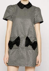 Kortärmad klänning i svart och silver houndstooth-mönster med svart satinkrage och stora svarta rosetter på framfickorna.
