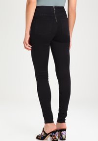 Högmidjade svarta jeans med dragkedja bak, med en slim fit och två bakfickor. Slät tyg med lätt stretch.