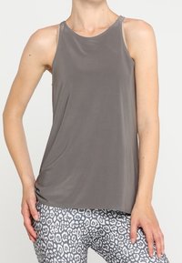 Top sin mangas gris de tela suave, con escote redondeado y corte relajado, combinado con leggings grises y blancos con estampado.