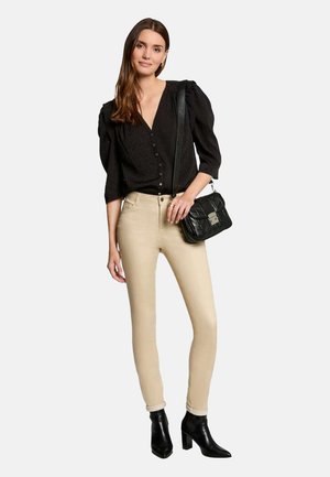 Top nero con bottoni e maniche a sbuffo, abbinato a jeans skinny beige e stivaletti neri alla caviglia. Gli accessori includono una borsa nera trapuntata.