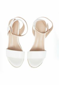 Sandali bianchi con tacco piatto, dotati di una fascia larga sulla punta e di un sottile cinturino alla caviglia. Materiale sintetico liscio con soletta beige.