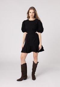 Black puff-sleeve dress with ruffled hem and side cut-outs. Worn with brown suede cowboy boots featuring embossed detailing.