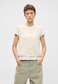 Κρεμ χρώματος, ριγέ γιλέκο με στρογγυλή λαιμόκοψη και κοντά μανίκια, που διαθέτει πέντε κουμπιά κατά μήκος του μπροστινού μέρους. Ελαφρύ πλέγμα υφάσματος.