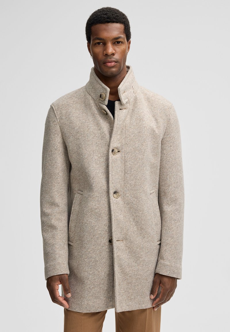 Beige herringbonejas met hoge kraag, knoopsluiting en zijzakken, gemaakt van een gestructureerde wolmixstof. Getailleerde pasvorm.