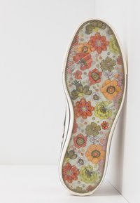 Semelle de chaussure avec un motif floral multicolore aux tons orange, jaune, vert et rose sur un fond blanc.