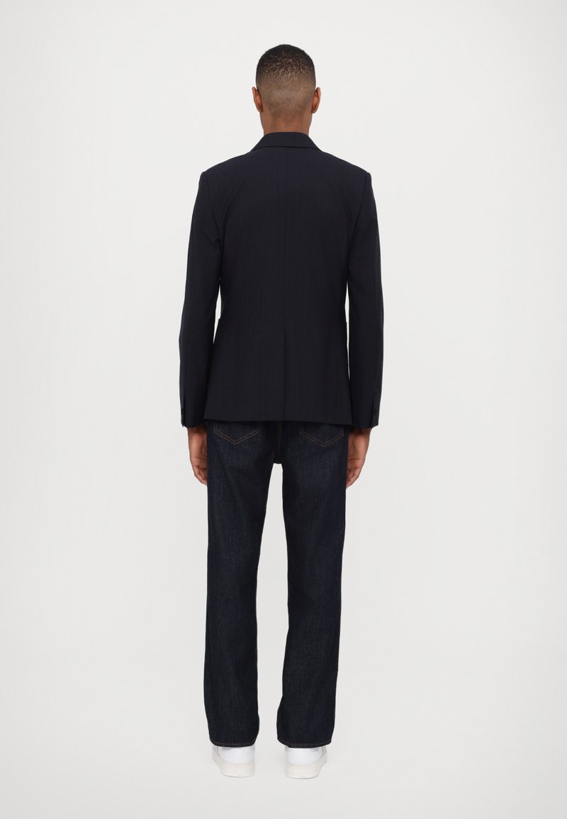 Navyblau taillierter Blazer mit einem glatten, strukturierten Design, kombiniert mit dunklen Jeans. Der Blazer verfügt über einen einfachen Schlitz und scharfe Revers.