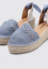 Espadrille de lona azul tejida con punta cerrada, suela de yute y tiras de tela en el tobillo. Presenta patrones intrincados y costuras en contraste.