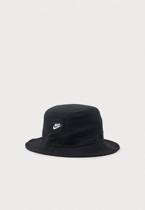 Chapeau seau Nike noir avec un large bord et une étiquette logo blanche à l'avant, présenté sur un fond blanc uni.