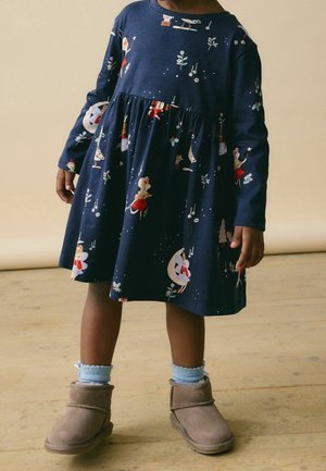 Robe bleu marine à manches longues avec une jupe froncée ornée de personnages imprimés, associée à des bottines grises et des chaussettes côtelées bleu clair.