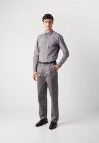 Camicia a maniche lunghe grigia, con chiusura a bottoni, taglio aderente, abbinata a pantaloni grigi coordinati, completata da una cintura e scarpe nere. Tessuto dalla superficie liscia.