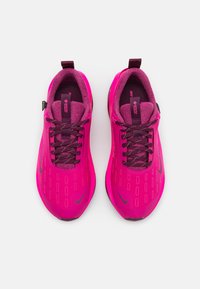 Baskets de sport roses avec une tige texturée, un design façonné, des lacets et une semelle extérieure noire. Présente des accents roses foncés contrastants et un branding.