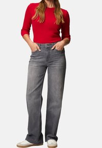 Rotes Langarmshirt kombiniert mit hellgrauen, weiten Jeans. Die Jeans haben eine mittelhohe Taille und sind mit Vordertaschen gestaltet.