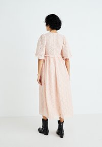 Vestido de encaje rosa con un patrón de diamantes, mangas cortas abullonadas y una falda fluida. Combinado con botines negros, creando un contraste en el estilo.