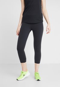 Svarta capri leggings med en åtsittande design och slät yta, tillsammans med ljusgröna träningsskor. Enkla stickningar som accentuerar.