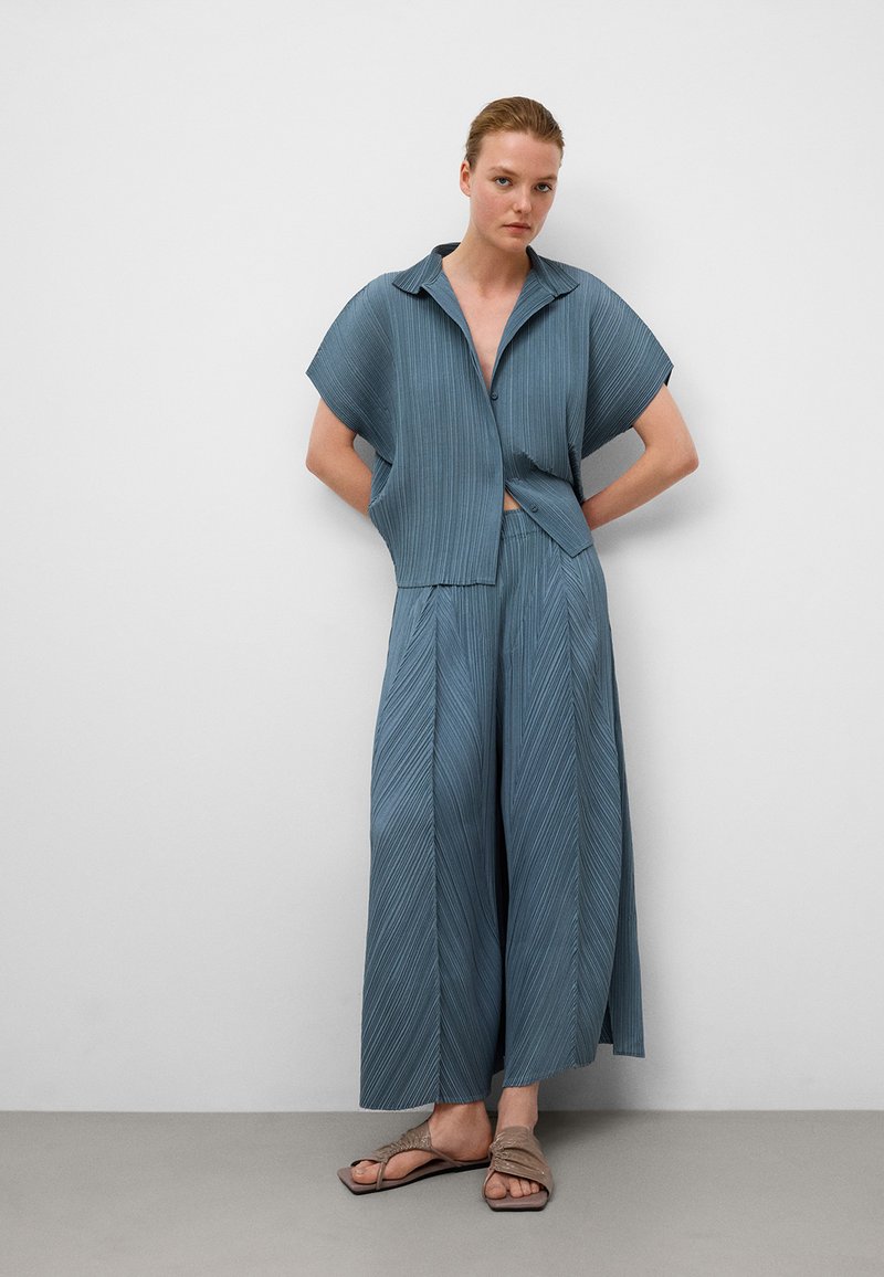 Completo due pezzi azzurro chiaro con pieghe composto da giacca a maniche corte e pantaloni a gamba larga. Tessuto testurizzato con una vestibilità rilassata.