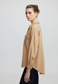 Beige striped shirt with buttoned cuffs and a breast pocket. Features a collar and loose fit, made of a lightweight fabric.
