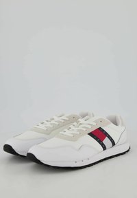 Sneakers atletici bianchi con accenti beige, caratterizzati da strisce orizzontali rosse e blu navy sul lato e una suola in gomma nera. Design con lacci frontali.