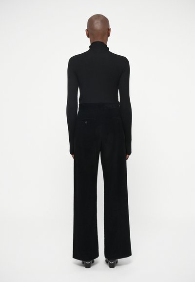 Fitted black turtleneck paired with wide-leg black corduroy pants featuring a textured surface and back pockets. Simple, tailored design.